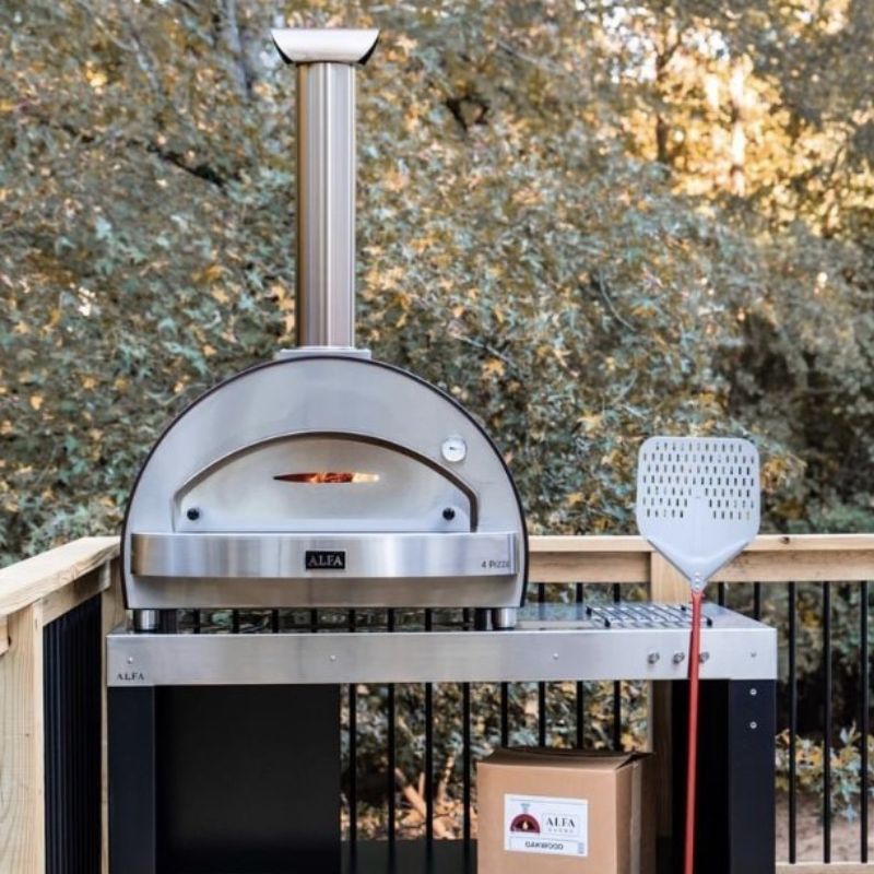 Outdoor Alfa 4 Italian pizza oven with a premium pizza peel on a wooden deck against a tree background | Alfa 4 Pizze Sale