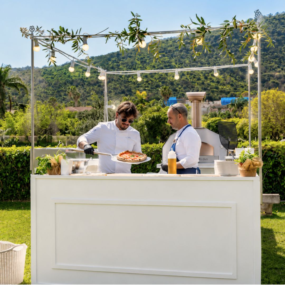 Chefs preparing freshly baked pizza from an ItaliaForno Grande Pro Duo Hybrid Pizza Oven at a backyard garden setting for an event