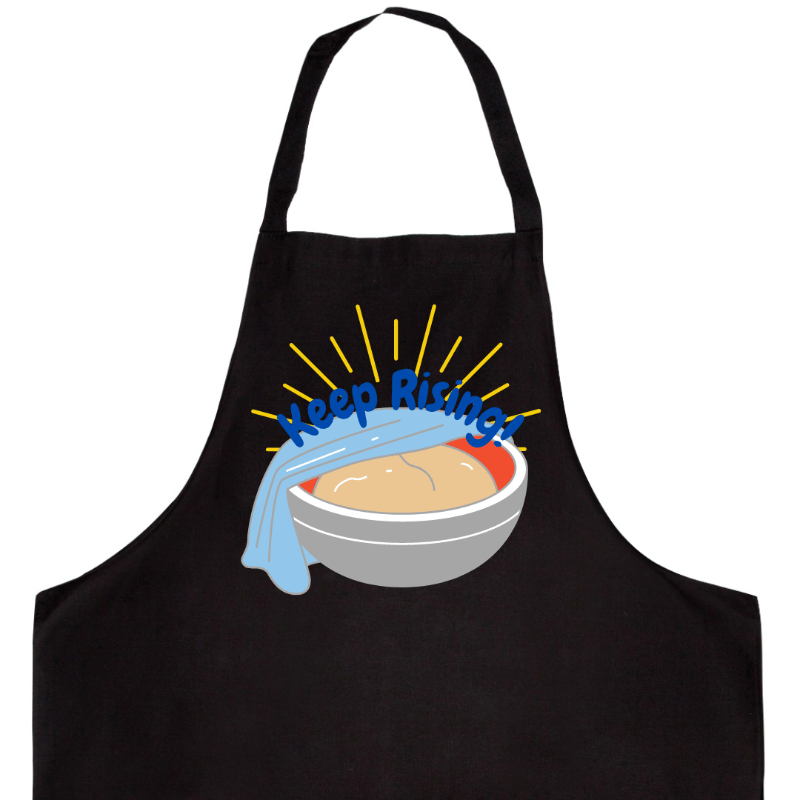 upclose photo of black apron featuring the design &quot;proofing bowl with phrase keep rising&quot; on it