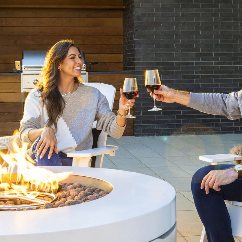 Friends enjoying a glass of wine in front of the weather-resistant outdoor Ledge Halo Fire pit in a modern patio