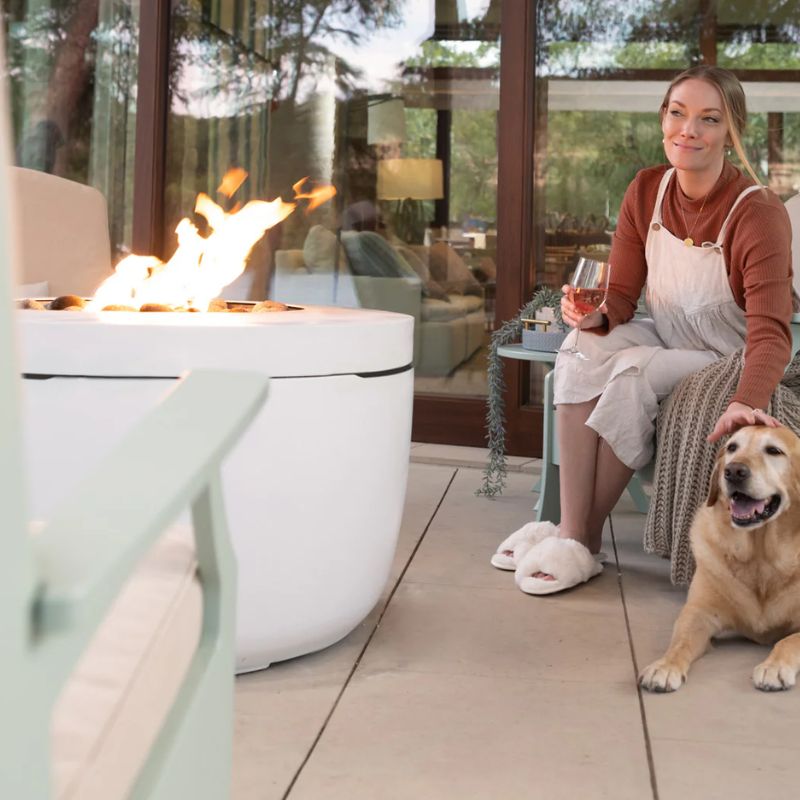 Woman and her dog sitting in front of the Ledge Halo LP Gas Fire Pit in a modern patio