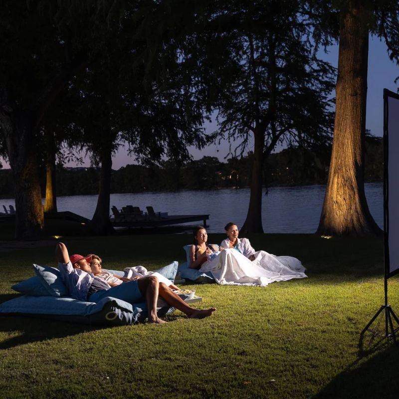A couple of friends watching a movie outdoors on the grass using the versatile Laze PIllow