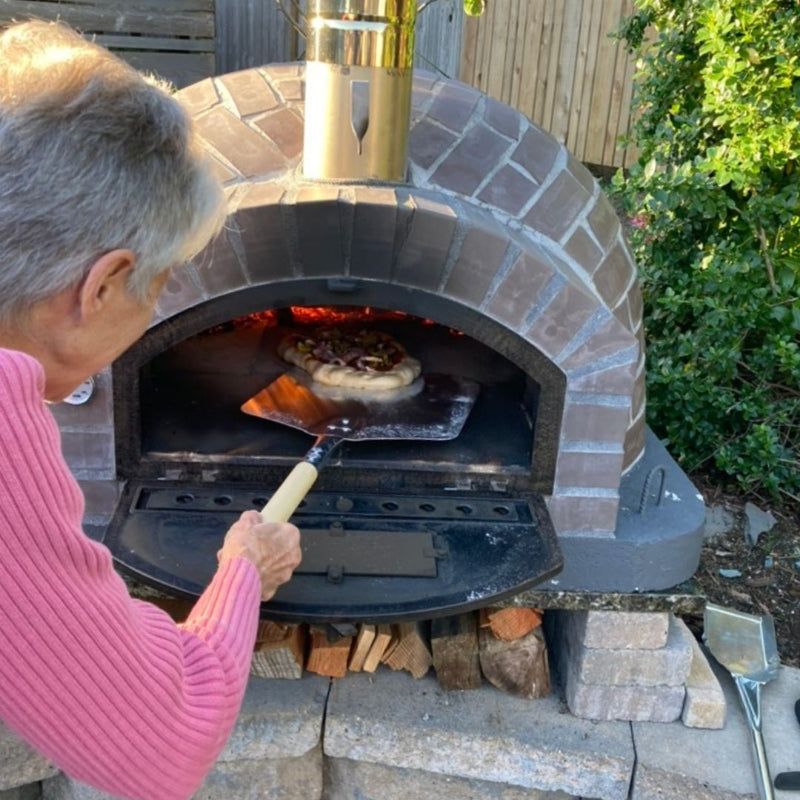 Woman launching a pizza inside of the Lume Largo Tudo Wood Fired Authentic Pizza Oven