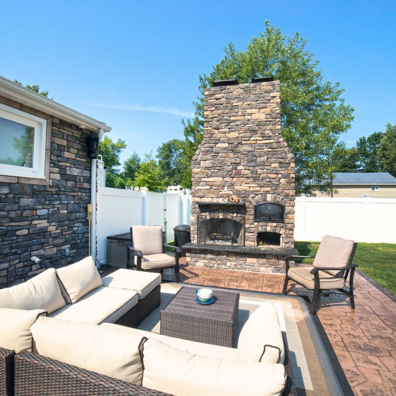 Round Grove Brick Oven installed next to a fireplace in outdoor sitting area